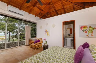 a bedroom with a bed and a chair and windows at Exclusive Villa Tanager Ocean View w AC Private pool terrace in Quepos