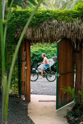 a man riding a bike with a surfboard on it at Iluminar Beachfront Suites in Nosara