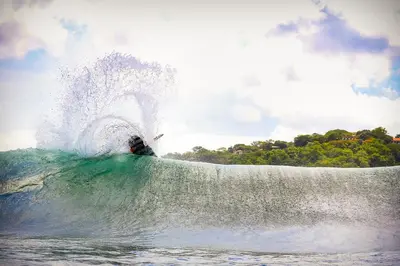 a person riding a wave on a surfboard in the ocean at Iluminar Beachfront Suites in Nosara