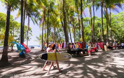 a woman carrying a surfboard on a beach with palm trees at Bamboo River House and Hotel in Dominical