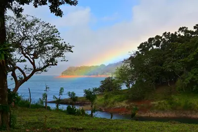 a rainbow in the sky over a lake with trees at Villa Corazón - private beach at Lake Arenal in Nuevo Arenal