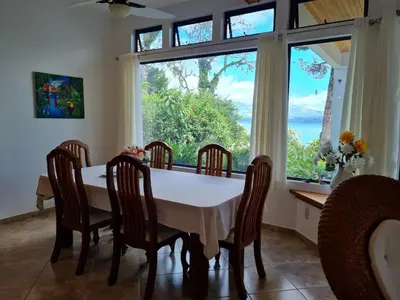 a dining room with a table and chairs and a large window at Villa Corazón - private beach at Lake Arenal in Nuevo Arenal