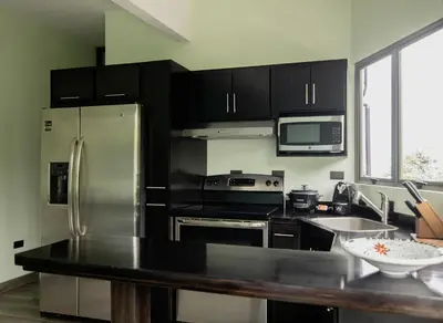 a kitchen with black cabinets and a stainless steel refrigerator at Palo Rosa in Quepos