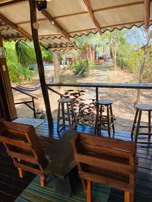 a porch with two chairs and a table and stools at Luminosa Uvita Hostel in Uvita