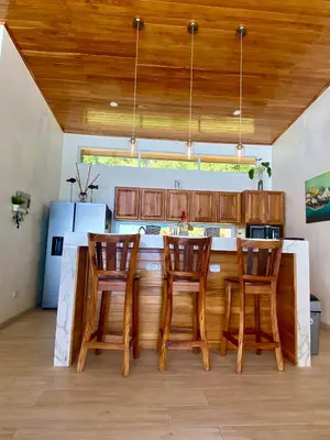 a kitchen with wooden cabinets and a counter with four chairs at Casa de Teak in Savegre