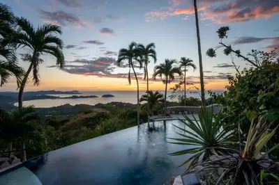 a swimming pool with palm trees and a sunset at Stunning Mountaintop Property with Stylish Main Home, Private Guesthouse & Infinity Pool in Santa Cruz