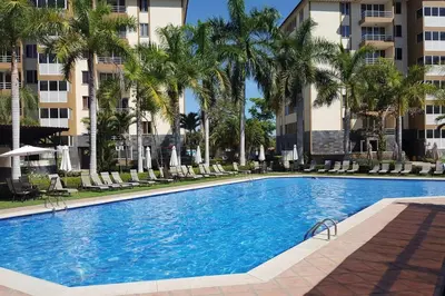 a swimming pool with chairs and palm trees and buildings at Oceanview 6th Floor Jaco Condo in Jacó