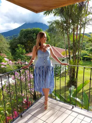 a woman in a blue and white dress standing on a balcony at Miradas Arenal Hotel & Hotsprings in Fortuna