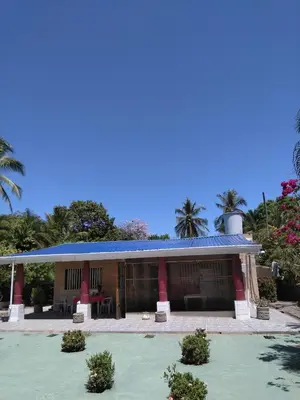 a building with a blue roof and palm trees at Maison du Bonheur CABALLO DEL MAR sur la plage avec bassin de rafraichissement in Parrita