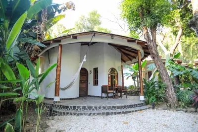 a small white house with a porch in a forest at Manala Hotel in Santa Teresa Beach