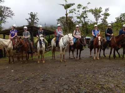 a group of people riding horses on a dirt road at Hotel Rio Celeste to Know in Rio Celeste