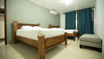 a bedroom with two beds with blue curtains and a chair at Coati Arenal Lodge in Fortuna