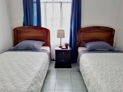 two beds in a bedroom with blue curtains and a window at Entire Homy apartment for you, 5 min SJO Airport in Alajuela City
