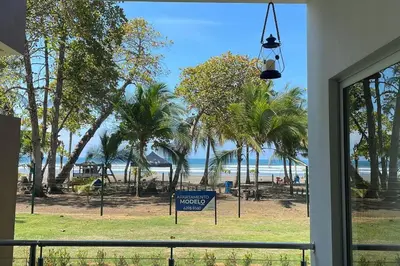 a view of a beach with palm trees and a sign at Bejuco Beachfront Condo FRENTE A LA PLAYA hermoso condominio NUEVO in Esterillos Este
