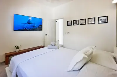 a white bedroom with a large bed with a tv on the wall at Villa Taleona in Santa Teresa Beach