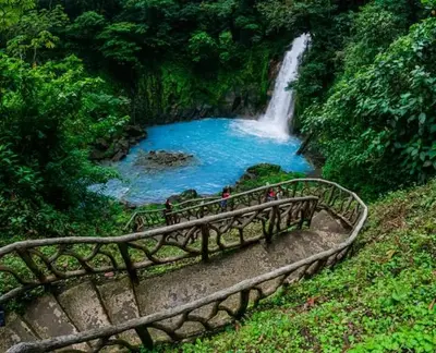 people standing on a bridge in front of a waterfall at Cabinas El Pilón Río Celeste in San Rafael