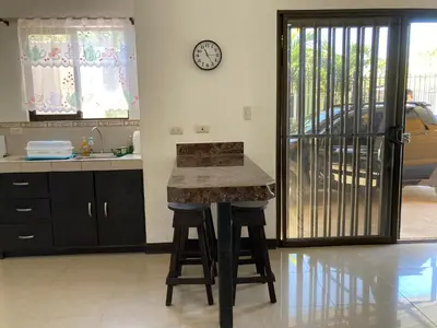 a kitchen with a counter with stools and a clock on the wall at Casa Binisa Fresca y agradable in Liberia