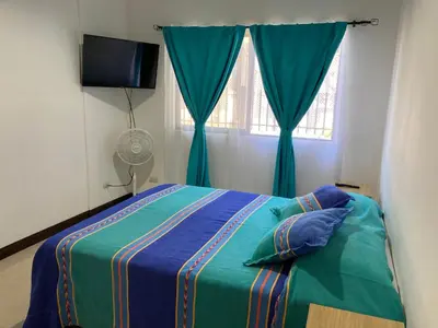 a bedroom with a bed with blue curtains and a window at Casa Binisa Fresca y agradable in Liberia