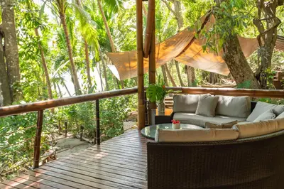a porch with a couch and a table and trees at Los Vivos Beachfront Experience in Pochote