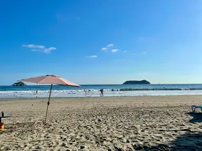 a beach with an umbrella and people in the water at Cabinas Chazu #2 in Quepos