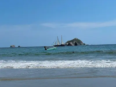a boat in the ocean with a beach and a boat at Cabinas Chazu #2 in Quepos