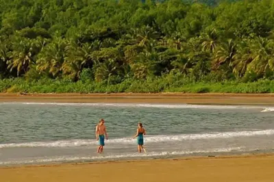 two people walking in the water on the beach at Bungalows Baobab in San Isidro