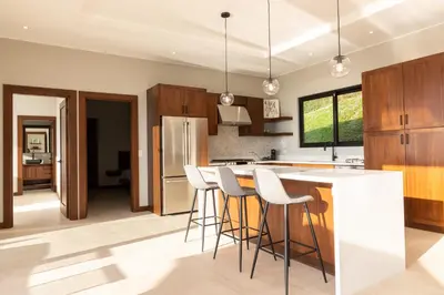 a kitchen with wooden cabinets and bar stools at Casa Solaz - by Pura Villas in Dominical