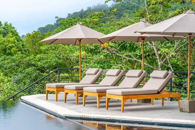 a group of lounge chairs and umbrellas next to a pool at Casa Amigos - By Pura Villas in Dominical