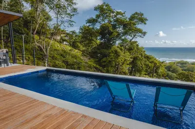 a pool with two chairs and the ocean in the background at Le Suite in Santa Teresa Beach