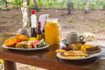 a table with a plate of breakfast foods and orange juice at Playa Ganadito Ecolodge in Drake