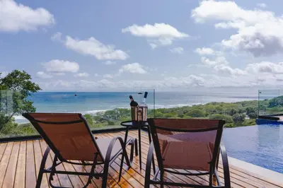 two chairs and a table on a deck with a view of the ocean at Casa Nina Santa Teresa in Santa Teresa Beach