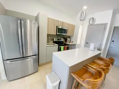a kitchen with a stainless steel refrigerator and wooden chairs at SUNSET OCEAN VIEW CONDO in Jacó