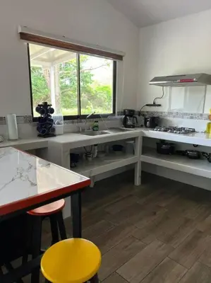 a kitchen with white counters and a yellow stool at Encantadora Casa Amapolas in Cóbano