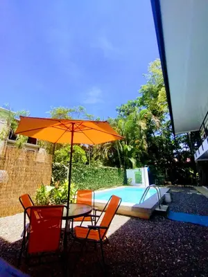 a table and chairs with an umbrella next to a pool at Casajungla Hostel in Jacó