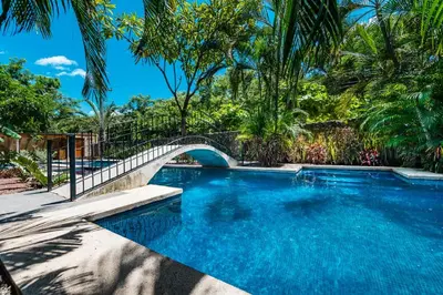 a swimming pool with a bridge in a resort at La Esquina (3 minutes from Beach, perfect for a family getaway) in Tamarindo