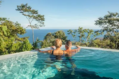 a man and woman sitting in a swimming pool in the water at Adeluna Luxury Villas in Montezuma