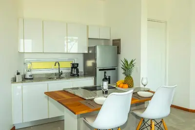a kitchen with white cabinets and a wooden table with white chairs at Adeluna Luxury Villas in Montezuma