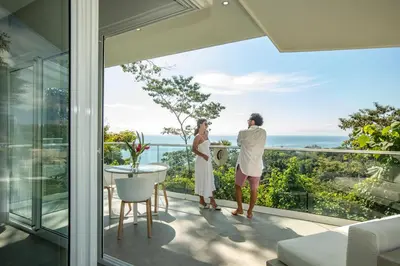 a couple standing on a balcony looking out at the ocean at Adeluna Luxury Villas in Montezuma