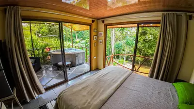 a bedroom with a bed and a balcony with a tub at Bungalows Las Iguanas Arenal Volcano in Fortuna