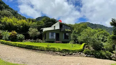 a green house on a hill with a yard at Villa Golondrina Cabaña rodeada de Naturaleza in Monteverde Costa Rica