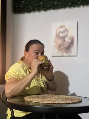 a woman sitting at a table eating a hamburger at Zeus Guest house & Car Rental Free SJO Airport Shuttle-NATIONWIDE PRÍVATE SHUTTLE SERVICE in La Garita