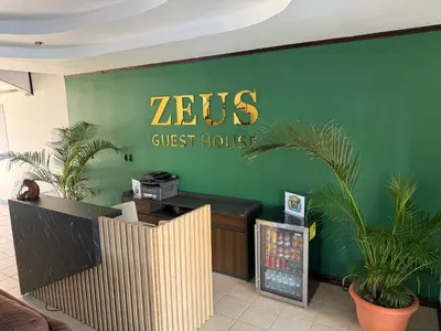a zeus guest house sign on a green wall at Zeus Guest house & Car Rental Free SJO Airport Shuttle-NATIONWIDE PRÍVATE SHUTTLE SERVICE in La Garita