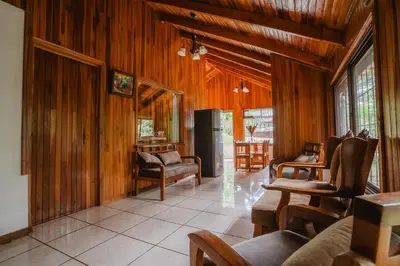 a living room with wood paneled walls and a room with chairs at Cabañas La Pradera in Monteverde Costa Rica