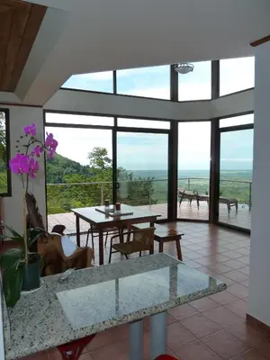 a living room with a table and chairs and windows at Casa Altamar in Jacó