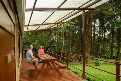 a man and woman sitting at a picnic table on a deck at Los Pinos Cabins & Reserve in Monteverde Costa Rica