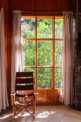 a wooden rocking chair sitting in front of a window at Los Pinos Cabins & Reserve in Monteverde Costa Rica