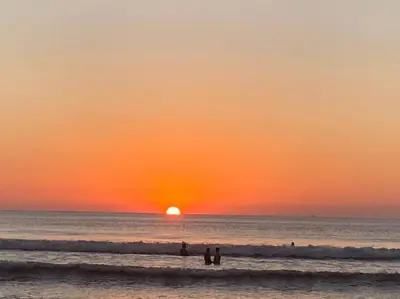 a sunset on the beach with people standing in the water at Loft 45 in Playa Hermosa, paradise near the ocean! in Playa Hermosa