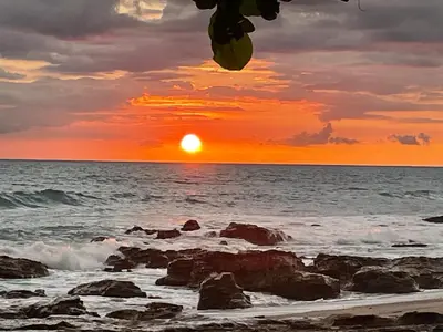 a sunset on the beach with rocks and the ocean at Garza Tigre Apartamentos in Cóbano