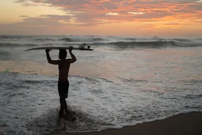 a man standing in the ocean with a surfboard on his head at Hotel Guiones in Nosara