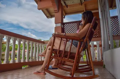 a woman sitting in a rocking chair on a porch at Hotel Sierra Arenal in Fortuna